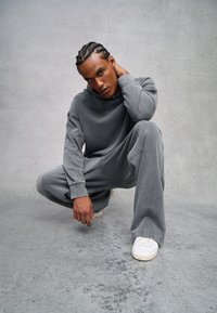 Grau Hoodie und passende Jogginghose aus weichem Material, mit lockerer Passform und minimalen Nähten, ergänzt durch weiße Sneaker.