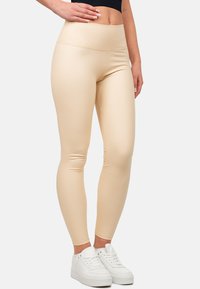 Leggings beige realizzati in materiale elastico con vita alta, caratterizzati da una texture liscia e dettagli di cucitura sottili, abbinati a sneaker bianche.