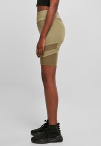 Jupe active beige taille haute avec panneaux latéraux en mesh et texture lisse, associée à des chaussures montantes noires à lacets pour un contraste.