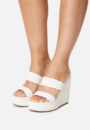 Valkoiset kiilakorkosandaalit, joissa on kudottu pinta, kahdet hihnat jalan yli ja tukeva pohja. Avoin varvasosa, joka korostaa luonnollisia kynsiä.