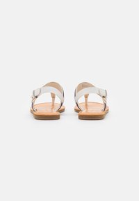 Hvide lædersandaler med flerfarvede mønstrede stropper, åben ryg, flad sål, justerbar ankelspænde og en glat tan indersål.