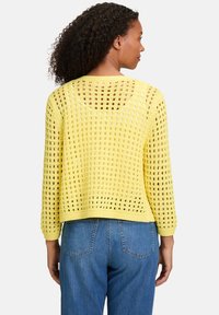 Pull en maille jaune avec un tissage lâche, manches trois-quarts et coupe courte, associé à un jean en denim. Motif ouvert texturé.