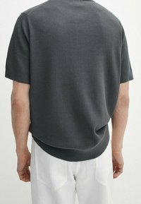 Maglietta a maniche corte grigio scuro in maglia con vestibilità rilassata, texture a coste e orlo curvo, abbinata a pantaloni bianchi. Nessun marchio visibile.