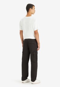 Hvid kortærmet t-shirt parret med sorte cargo-bukser med sidelommer og en afslappet pasform. Hvide sneakers fuldender looket.