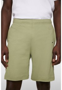 Jasnozielone bawełniane szorty z elastycznym pasem, zszytymi brzegami i małym czarnym logo z przodu po lewej stronie.