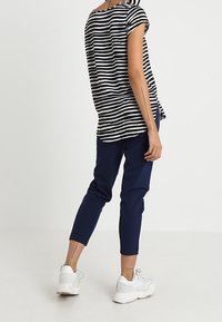 Černobíle pruhované tričko s krátkým rukávem, zkombinované s tmavě modrými úzkými kalhotami a bílými teniskami, které ukazují uvolněný, neformální styl.