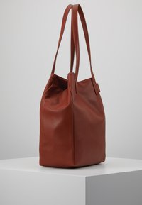 Rode leerachtige tote bag met twee lange handvatten; afgeronde vorm met een platte bodem; heeft subtiele plooien voor een ontspannen uiterlijk.