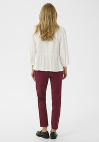 White peplum blouse with long sleeves, paired with maroon slim-fit pants and black flat shoes, viewed from the back.
