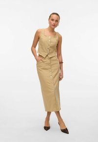 Gilet court beige avec encolure carrée et boutons sur le devant, associé à une jupe longue à boutons sur le devant avec poches latérales et texture subtile.
