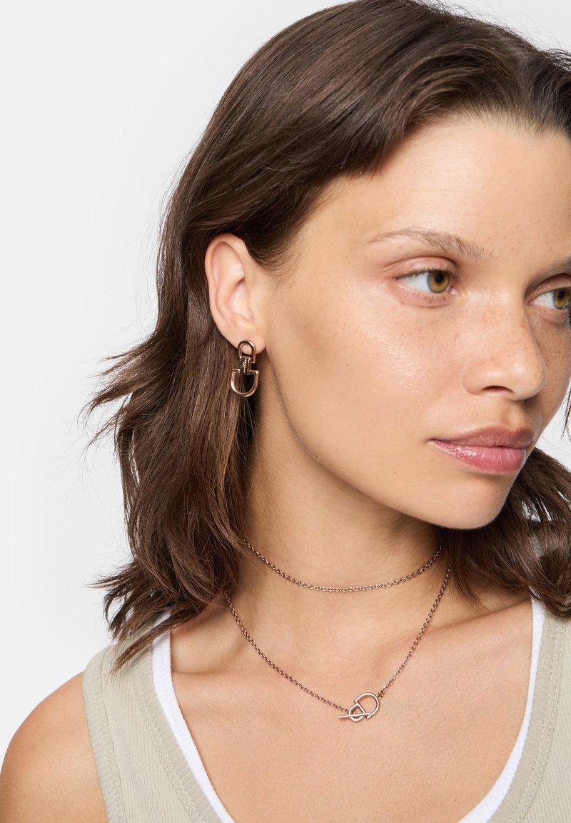 Ohrringe aus bronzefarbenem Metall mit einem geometrischen Schlossdesign; schichtige metallic Kettenhalskette mit einem verwobenen Akzent.