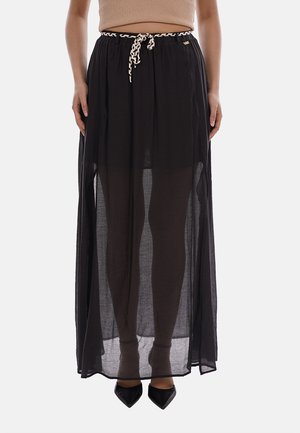 Gonna lunga nera trasparente con cintura arricciata e coulisse a contrasto, indossata con scarpe nere appuntite e top beige corto.