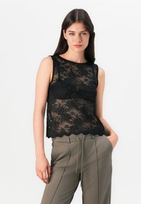 Crop top en dentelle noire avec un motif floral, texture transparente et ourlet festonné. Porté avec un pantalon taille haute vert olive.