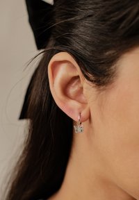 Orecchino a forma di farfalla in argento, con dettagli di incisione intricati sulla farfalla, appeso a un piccolo cerchio, mostrato sull'orecchio di una persona.