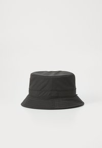Chapeau seau noir en tissu texturé, avec un large bord et une bande cousue autour de la base. Design minimaliste, sans motifs ni accents.