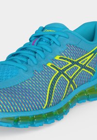 Chaussure de course bleue avec mesh rayé multicolore, logo jaune néon, lacets bleus et semelle coussinée transparente verte.