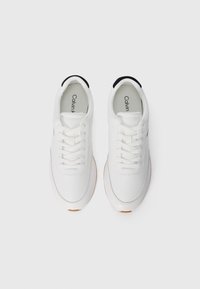 Weiße Sneakers mit Schnürsenkeln, hergestellt aus glattem Synthetikmaterial. Verfügt über eine schwarze Fersenlasche und eine orange Gummisohle mit abgerundetem Zehendesign.