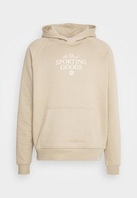 Béžová mikina s kapucí, která má přední kapsu, žebrované manžety a stahovací šňůrku na kapuci. Na přední straně je bílý nápis "Les Deux SPORTING GOODS".