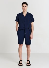 Navyblaues kurzärmliges Hemd mit strukturiertem Muster, Knopfverschluss; passende navyblaue Shorts mit Kordelzug; schwarze Sandalen. Einfaches und funktionales Design.