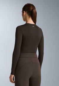 Hnedý dlhý rukáv top s diamantovým vzorom a priliehavým strihom, kombinovaný s vysokými legínami v zodpovedajúcej farbe. Hladká textúra.