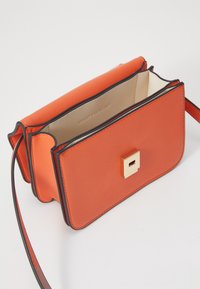 Borsa a tracolla in finta pelle arancione con dettagli neri a contrasto, hardware quadrato dorato e un interno aperto foderato in beige chiaro.