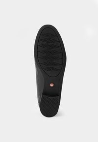 Semelle de chaussure noire en caoutchouc texturé, avec une surface de préhension à motif et un petit détail rouge près du talon. Bords lisses, forme ovale.