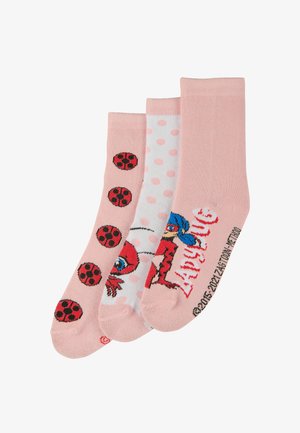 Drei Paar Socken in Pink und Weiß. Eines hat rote Marienkäfermuster, ein anderes zeigt pinke Pünktchen, und das dritte zeigt ein Charakterdesign.