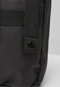 Primer plano de tela de nylon negra con un botón a presión negro en una correa con lazo, parte de una bolsa o mochila.