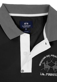 Camisa polo negra ajustada con cuello gris, tapeta de botones blanca y un logotipo bordado con jinetes. Tejido de mezcla de algodón.