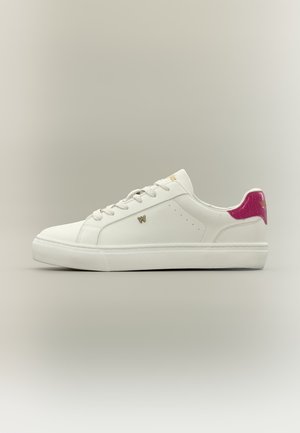 Λευκό χαμηλό αθλητικό παπούτσι με λευκά κορδόνια, χρυσό λογότυπο "W" στο πλάι και έντονη ρόζ υφασμένη ταμπέλα στη φτέρνα, σε ουδέτερο φόντο.