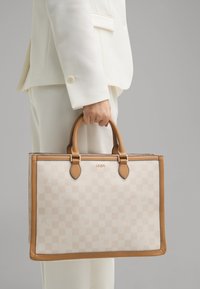 Sac fourre-tout à carreaux beige avec des accents et des poignées en cuir tan. Présente le nom de la marque en doré. Forme rectangulaire structurée.
