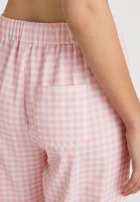 Pants met een roze en witte ruitprint hebben een elastische tailleband en een achterzak. Het materiaal lijkt zacht en lichtgewicht.