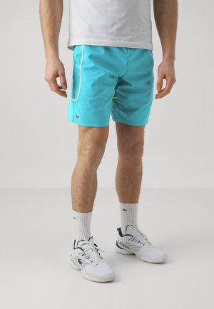Un short de bain turquoise en matériau léger avec des garnitures blanches. Comprend une poche latérale et un petit logo vert sur l'ourlet.