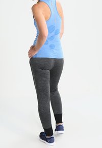 Niebieski bezrękawnik sportowy o lekkim połysku, zestawiony z dopasowanymi szarymi spodniami dresowymi z czarnymi mankietami i teksturowanym wykończeniem.