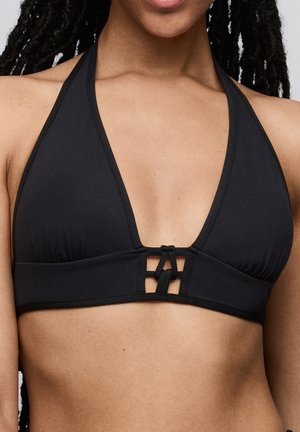 Vrouw draagt een zwarte halterbikinitop met een decoratieve knoopdetail in het midden aan de voorkant.