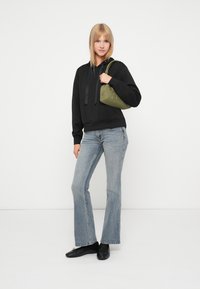 Svart hettegenser med snøring, lyseblå vide jeans og svarte ballerinas. Bærer en grønn håndveske med nagler og rund form.