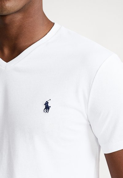 Biały bawełniany T-shirt z dekoltem w serek, z granatowym haftowanym logo jeźdźca na lewej piersi. Tkanina ma gładką fakturę.