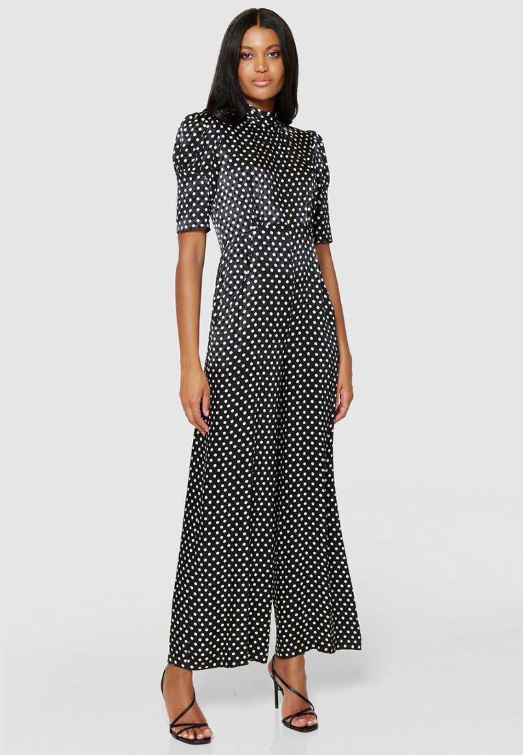 Czarny kombinezon w białe kropki z krótkimi, bufiastymi rękawami, dopasowanym fasonem i szerokimi nogawkami, wykonany z gładkiego, strukturalnego materiału.