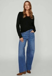 Sweater preto de manga longa com decote em V, combinado com jeans azuis de perna larga e cintura alta e botins castanhos de salto. Texturas suaves, ajuste casual.