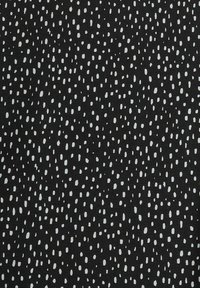 Černá látka s abstraktním vzorem rozptýlených bílých teček, které se liší tvarem a velikostí, s hladkou strukturou.