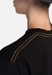 Black t-shirt featuring gold decorative stitching along the shoulder seam; smooth texture with a classic fit and crew neck design.
