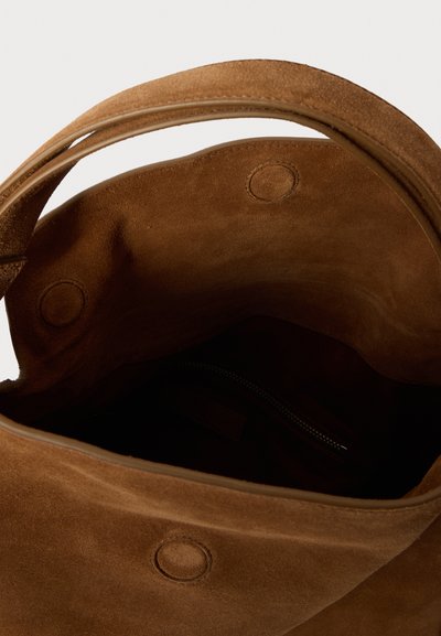 Ruda zomšinė rankinė su erdviu vidumi, turinti užtrauktukų kišenę ir du apvalius spaustukus uždarymui. Lygi tekstūra, švelnūs kraštai.