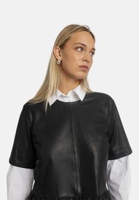 Schwarzes Lederoberteil mit kurzen Ärmeln, darunter ein weißes kragenloses Hemd und ein geraffter Saum, glatte Textur und minimale Nähte.