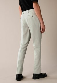 Light grey trousers made of linen, featuring a straight cut, two back pockets with buttons, and a smooth texture. Worn with black shoes.