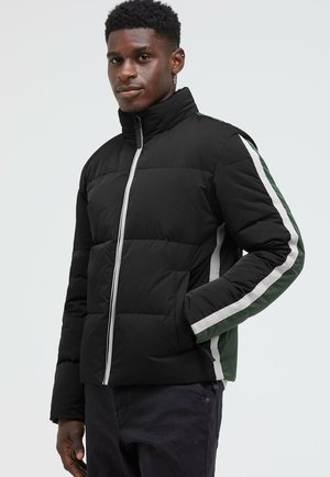 Schwarze gepolsterte Jacke mit hohem Kragen, ausgestattet mit grünen und weißen Seitenstreifen sowie einem Reißverschluss auf der Vorderseite. Strukturierter, robuster Stoff.