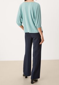 Top azzurro chiaro, oversize, con maniche a sbuffo, abbinato a pantaloni navy a gamba larga. Tessuto morbido con una vestibilità rilassata e scollatura leggermente rotonda.