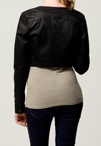 Svart kort läderjacka med knäppta ärmslut, med en enkel rund halsringning och slät textur, lagd över en ljusbeige topp.