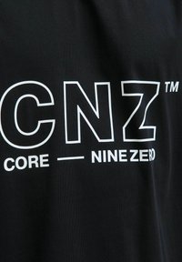 Sort bomulds-t-shirt med stort hvidt tekst: "CNZ™ CORE — NINE ZERO" i fed og enkel typografi på forsiden.
