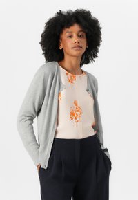 Gray cardigan with a ribbed neckline and buttons, worn over a floral-patterned blouse with orange details, paired with dark trousers.