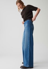 Weite Jeans aus blauem Denim mit hoher Taille, ausgestattet mit zwei Gesäßtaschen und dezenten Steppdetails. Glatte Textur mit klassischem Knopfverschluss.