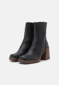 Bottes chevilles en cuir noir avec un bout carré et un talon épais en bois. Dotées d'une fermeture éclair latérale et d'une semelle texturée pour une meilleure adhérence.